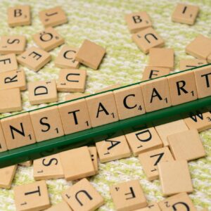 Wooden Scrabble tiles spelling 'INSTACART' on a green holder with scattered tiles.