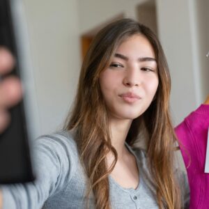Young woman taking a selfie with a new shirt indoors, showcasing the latest fashion.